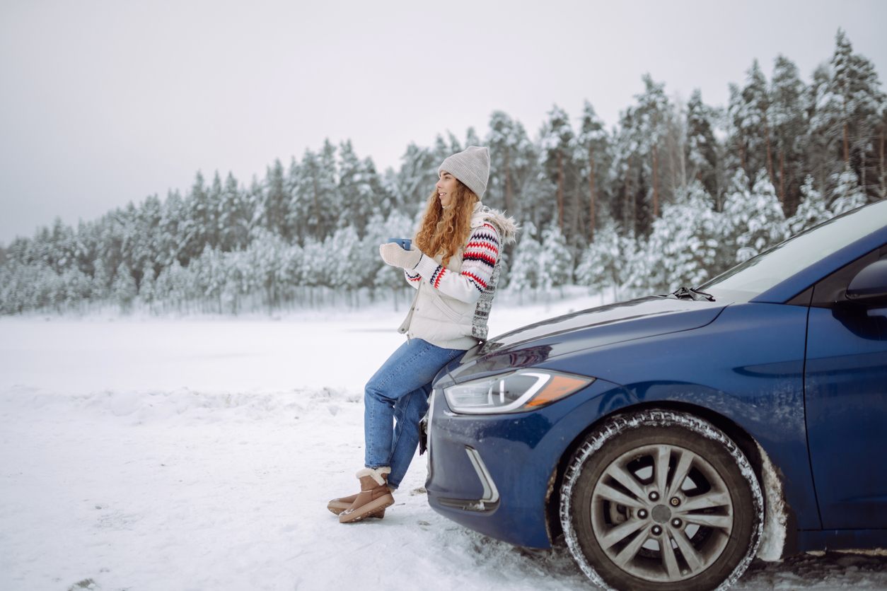 A woman leans on the hood of her car, enjoying the winter weather. 